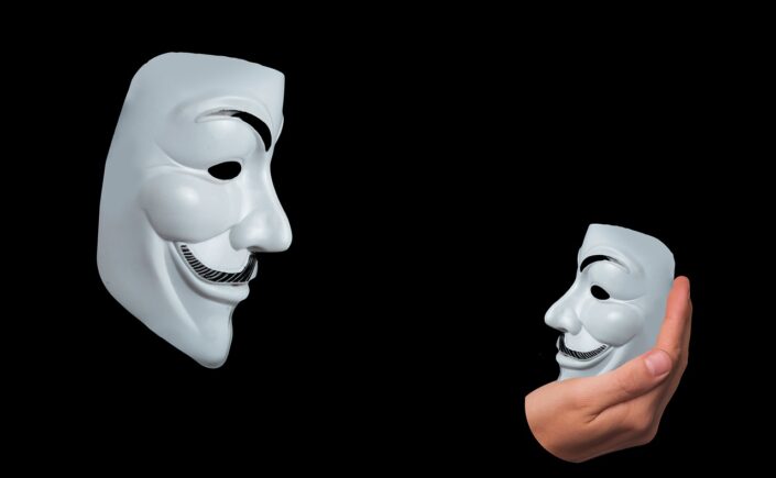 picture of a man in Guy Fawkes mask looking at a smaller Gur Fawkes mask in his right hand